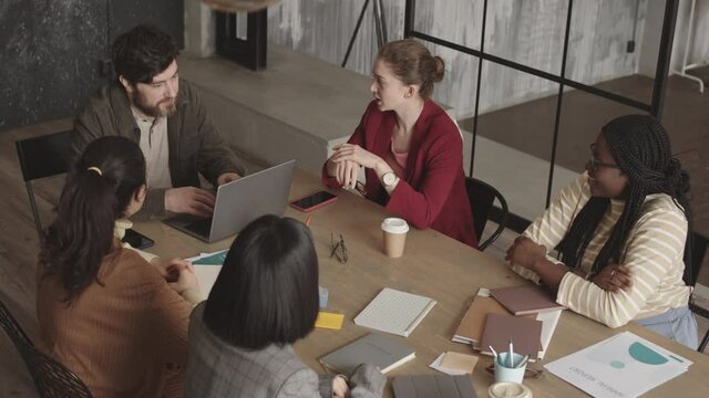 High-angle shot of female and male multiethnic colleagues sitting at conference table, talking, having business meeting, having discussion, laughing