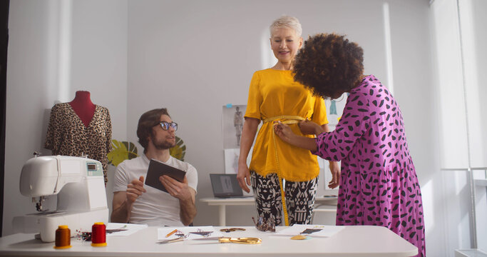 Fashion stylist sewing for private client and fitting clothes in workshop