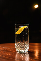 Gin and tonic cocktail in a highball glass served over ice, lemon twist garnish, at the wooden table at the bar, with copy space.
