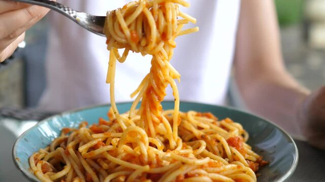 Close up of young blonde woman with nose piercing eating tomato pasta with great appetite 