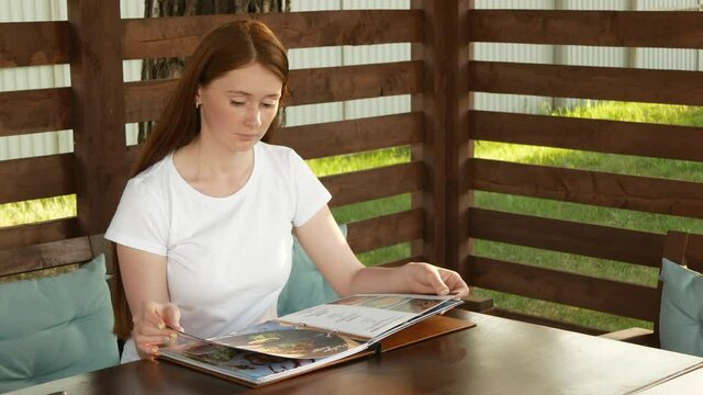 Attractive woman looks menu in summer cafe. Beautiful woman chooses dishes for dinner.