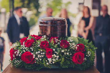 Funerary urn with ashes of dead and flowers at funeral. - obrazy, fototapety, plakaty