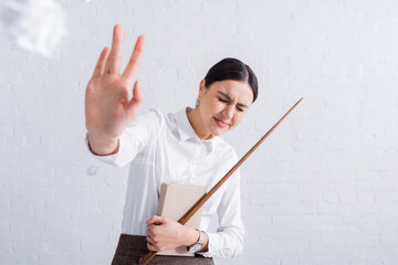 Teacher with pointer and book showing stop gesture near crumpled paper