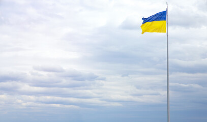 Ukraine flag against a blue sky with clouds. Banner for inserting text about the freedom and independence of European country.