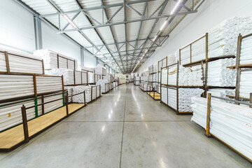 Spacious light interior of a large warehouse in a factory with special racks and shelves and products placed on them.