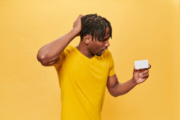 Handsome Afro Man Posing Over Yellow Background wearing yellow T-shirt keeping mock up credit card