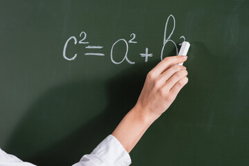 Cropped view of teacher writing equation on chalkboard