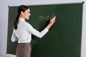 Smiling teacher writing mathematic equation on chalkboard