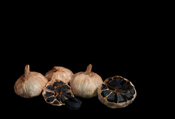 three whole bulbs of black fermented garlic and one cut crosswise isolated on black
