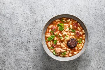 Spanish fabada with haricot, morcillas or blood sausage on gray stone table. View from above. Copy space. Asturiana traditional cuisine.