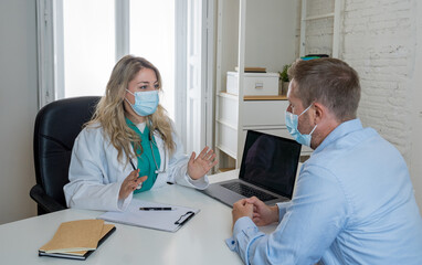 Happy female doctor and patient wearing protective face mask having a consultation in clinic office