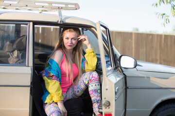 Beautiful girls in the style of the 90s sits in an old car.