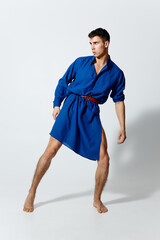 a handsome man in a woman's dress went to the side on a light background brunette full growth