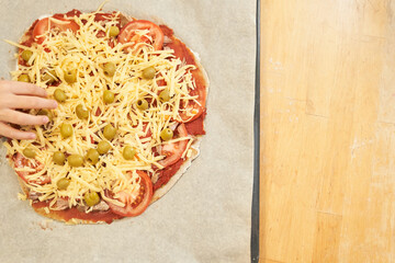 Childs hand with Pizza on baking paper prepared for baking. Healthy gluten-free pizza. Gluten-free cooking class. Photo with copy space. 