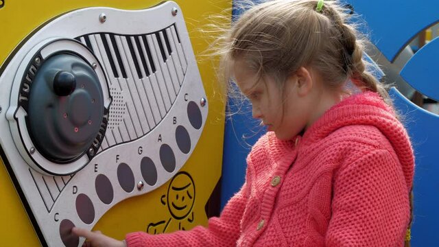 Interested blonde junior schoolgirl pretends playing piano on coloured wall of amusement park slow motion. Concept fun games