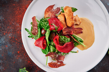 Warm salad with chicken and bacon on white plate on blue oxidized background. Dish for the menu. Top view