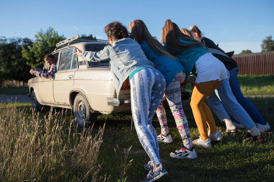 Young cheerful girls are pushing an old car. Women in the style of the 90s.