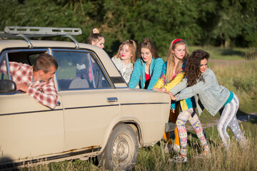 Young cheerful girls are pushing an old car. Women in the style of the 90s.