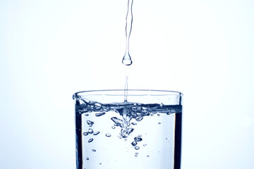 Jet of water or alcohol is pouring into a glass with splashes and bubbles, copy space