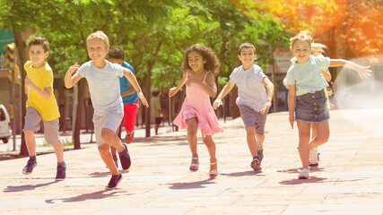 Obraz premium Team of positive kids running in race in the street and laughing outdoors