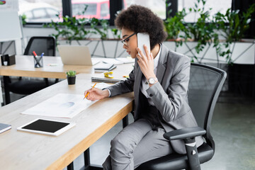 African american businesswoman talking on cellphone and holding pencil near document
