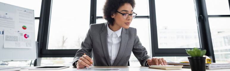 African american businesswoman using calculator near digital tablet and stationery, banner