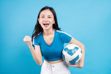 Beautiful Asian woman posing with soccer ball on blue background