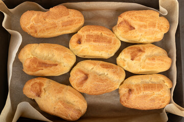 Cooking profiteroles, puffs, popovers, eclair. Fresh baked goods on baking sheet top view.