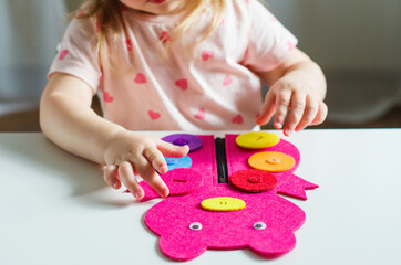 Little toddler girl buttoning a Montessori toy. Practical life skills, care of self, early...