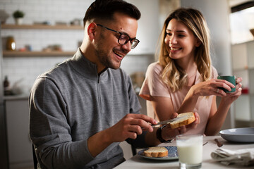 Beautiful young girl enjoying in breakfast with her boyfriend. Loving couple drinking coffee in the kitchen.