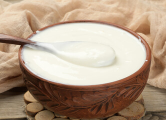 sour cream in a brown ceramic bowl with a wooden spoon on a wooden background, fermented milk useful product