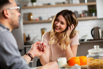 Beautiful young girl enjoying in breakfast with her boyfriend. Loving couple drinking coffee in the kitchen.
