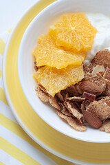 Whole grain oats and wheat flakes with orange, almond nuts and yogurt in a white bowl. Healthy morning breakfast concept close up	