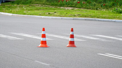 Macro shot of road traffic cones with orange and white stripes standing on street on gray asphalt during road construction works. Just painted white street lines on pedestrian crossing