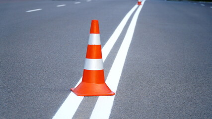 Macro shot of road traffic cones with orange and white stripes standing on street on gray asphalt during road construction works. Just painted white street lines on pedestrian crossing