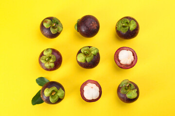 Fresh ripe mangosteen fruits with green leaves on yellow background, flat lay