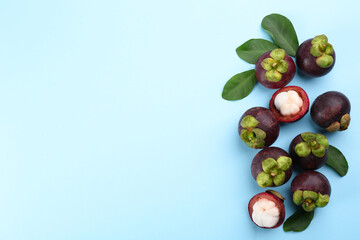 Fresh ripe mangosteen fruits with green leaves on light blue background, flat lay. Space for text