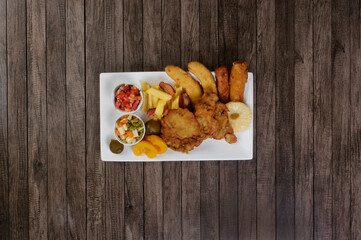 Cuban fillet. Made with Breaded Steak, Banana, Breaded Cheese and Ham. French Fries with Bacon. Vinaigrette, vegetables, and fruits. Served on the porcelain platter. Top shot. Vertical background.
