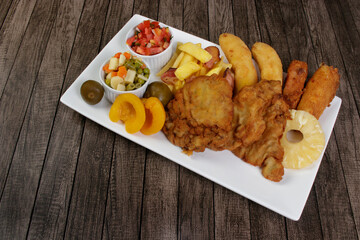 Cuban filet. Made with Breaded Steak, Banana, Breaded Cheese and Ham. French Fries with Bacon. Vinaigrette, vegetables, and fruits. Served on the porcelain platter. Close-up photo with space for text.