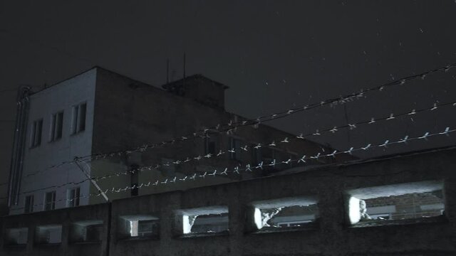 Prison Barbed Wire Over Concrete Fence Against Cloudy Sky At Cold Dark Winter Night During Snowfall. Incarceration, Jail, Restricted Area, Closed Zone, Security Concept