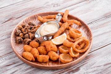 Beer snacks: fried wings, fried onion rings, french fries, cheese sticks, served with sauces on round board on wooden background. Photo for the menu and site. Space for text