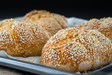 Fresh challah bread rolls hot from the oven on a baking tray. Gluten free bread buns or mini loaves with sesame seeds and golden color ready to eat. Fluffy shaped homemade bread on a dark background.