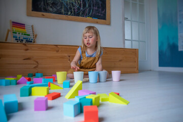 A little girl counts coins, plays with colorful circles and puts them in cups, a child learns to count and play in the classroom