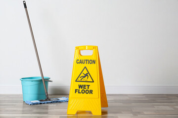 Safety sign with phrase Caution wet floor, mop and bucket indoors. Cleaning service