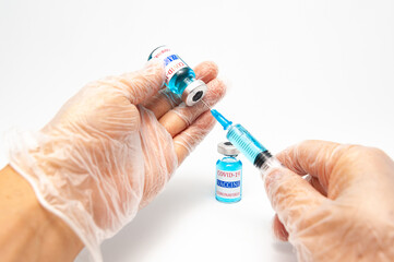 Medical concept - Close-up of hands with surgical glove holding syringe with needle and COVID-19 vaccine vial. Copy space. Isolated on a white background.