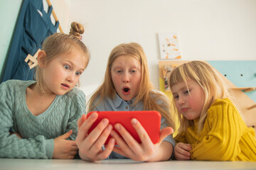 Children receive education at home in a classroom with a laptop, online courses for kids, three caucasian girls have fun and watch cartoons