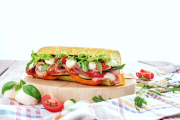 Fresh baguette sandwiches with ham, mozzarella cheese, tomatoes and fresh lettuce on wooden cutting board on light wooden background. Space for text