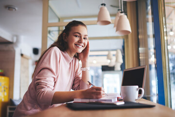 Fototapeta premium Cheerful woman writing in notebook during work