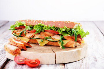 Fresh baguette sandwiches with chicken, cheese, tomatoes and fresh salad,on wooden cutting board on light wooden background.. Space for text