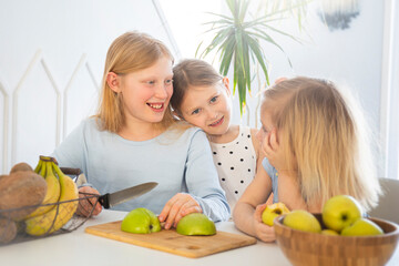 Fototapeta premium Children in the kitchen have fun and eat apples, kids cook breakfast together, cut an apple with a knife in a bright interior